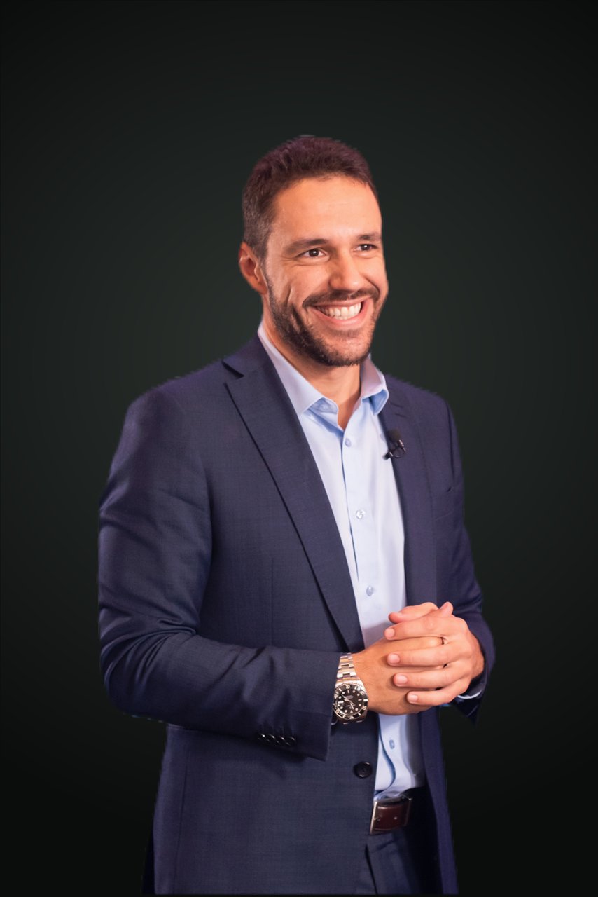 Professor Felipe Boselli, de terno azul-marinho e camisa azul-clara, sorrindo, em retrato sobre fundo escuro